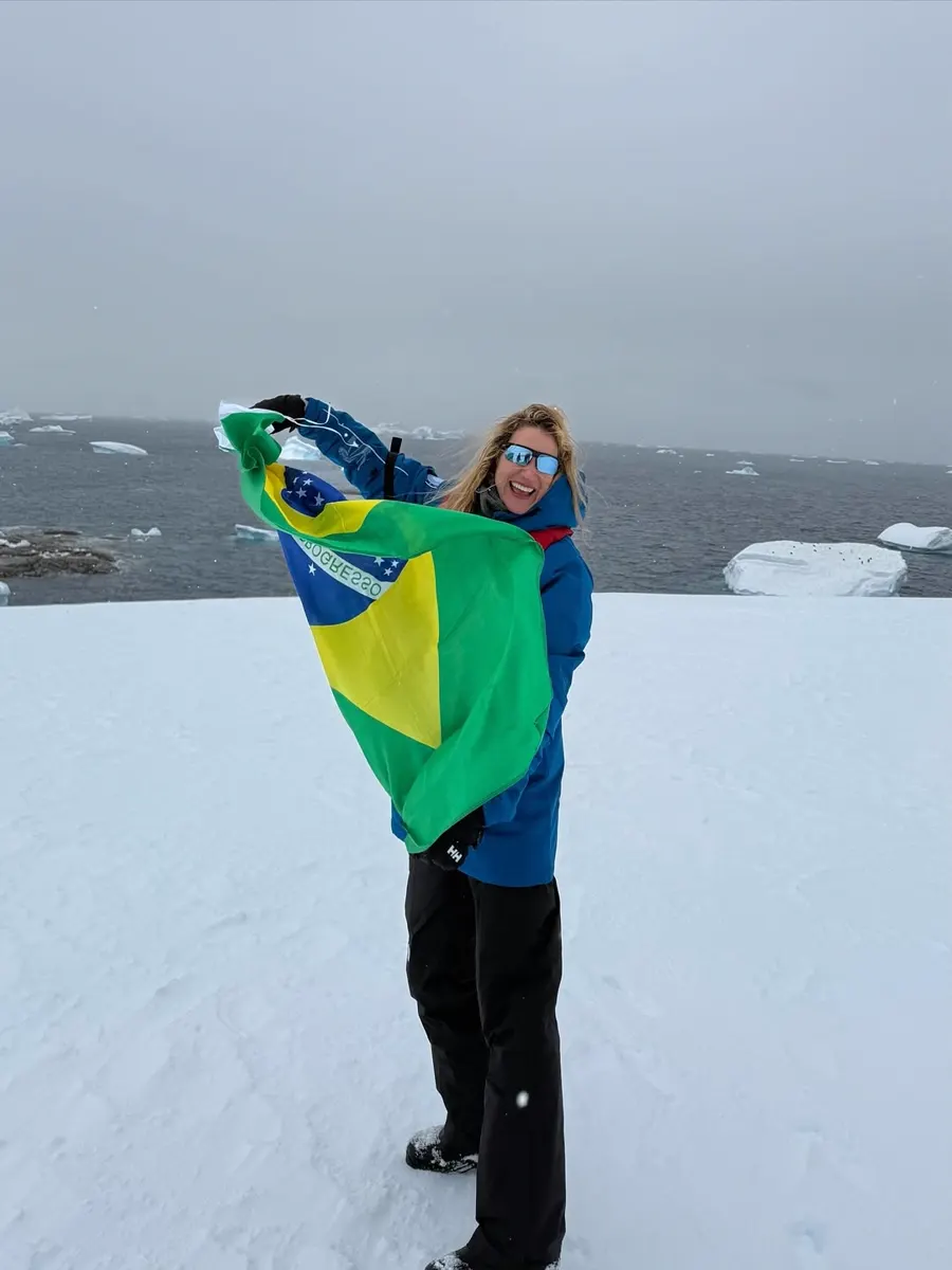 Gabriela Morais na Antártica segurando a bandeira do Brasil sobre a neve.